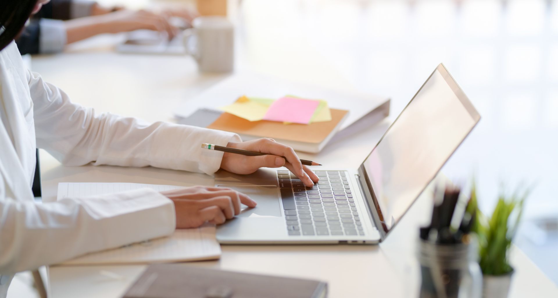 A imagem mostra uma pessoa usando um laptop para criar ou editar um currículo online. Ela está digitando, com materiais de escritório ao redor, em um ambiente claro e organizado.