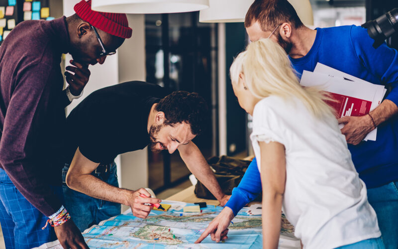 Grupo diverso colabora em mapa com marcadores, planejamento estratégico em equipe.