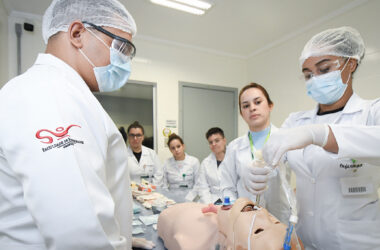 Estudantes do curso de Enfermagem da Unoeste participam de uma aula prática no Laboratório de Habilidades e Simulação, realizando procedimento de intubação em manequim de alta fidelidade sob supervisão, com equipamentos e materiais de suporte clínico dispostos na bancada.