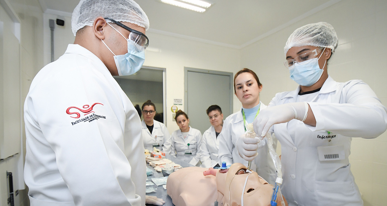 Estudantes do curso de Enfermagem da Unoeste participam de uma aula prática no Laboratório de Habilidades e Simulação, realizando procedimento de intubação em manequim de alta fidelidade sob supervisão, com equipamentos e materiais de suporte clínico dispostos na bancada.