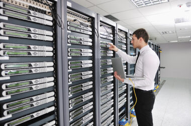 Homem vestido de calça preta e camisa branca trabalha em um servidor com Redes de Computadores