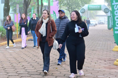 Pessoas caminham por uma área externa do campus da Unoeste, próximo à entrada sinalizada com bandeiras e arco institucional da universidade.