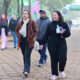 Pessoas caminham por uma área externa do campus da Unoeste, próximo à entrada sinalizada com bandeiras e arco institucional da universidade.