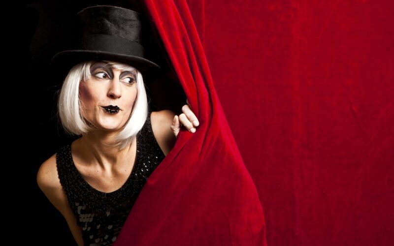 Artista de teatro espiando por trás de uma cortina vermelha no palco.