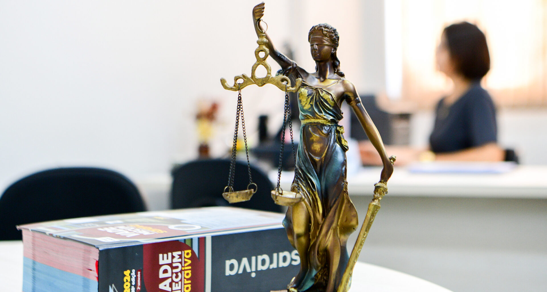 Vade Mecum ao lado da estátua da Justiça sobre uma mesa de estudos — representação simbólica do universo jurídico, que conecta os cenários das séries de advogados à escolha pelo curso de Direito.