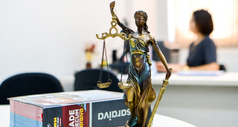 Vade Mecum ao lado da estátua da Justiça sobre uma mesa de estudos — representação simbólica do universo jurídico, que conecta os cenários das séries de advogados à escolha pelo curso de Direito.