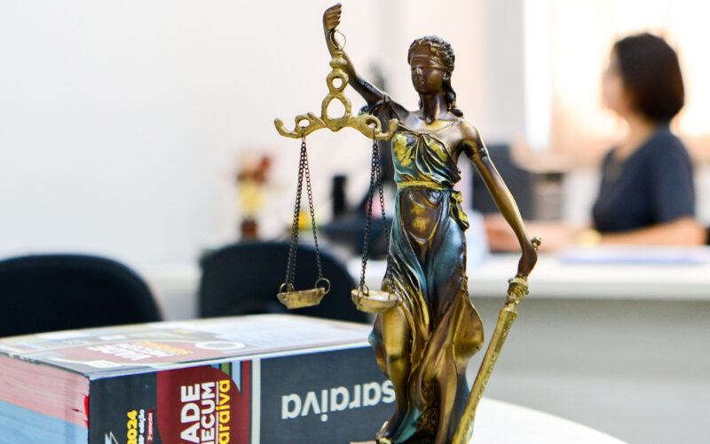 Vade Mecum ao lado da estátua da Justiça sobre uma mesa de estudos — representação simbólica do universo jurídico, que conecta os cenários das séries de advogados à escolha pelo curso de Direito.