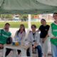 Estudantes universitários da Unoeste, em jalecos e coletes verdes, participam ativamente de um evento de extensão universitária ao ar livre. A imagem destaca o engajamento e a colaboração de alunos de ligas acadêmicas em iniciativas de voluntariado, exemplificando o aprendizado prático e a comunidade acadêmica.