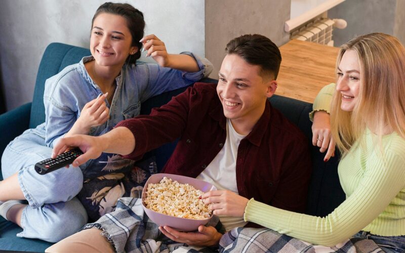 Grupo de jovens assistindo a filme em casa durante as férias, comendo pipoca e curtindo um momento de lazer.