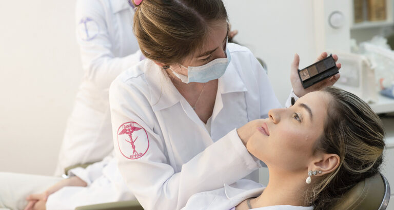 Estudante de Estética e Cosmética realizando procedimento de maquiagem facial em paciente durante atividade prática supervisionada, destacando técnicas profissionais de cuidado com a pele e embelezamento.
