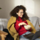 Mulher jovem sorridente, usando fones de ouvido e notebook no colo, comendo pipoca em uma poltrona confortável. Cena ideal para assistir a filmes sobre inteligência artificial em casa, desfrutando de entretenimento digital e o fascinante universo da IA.