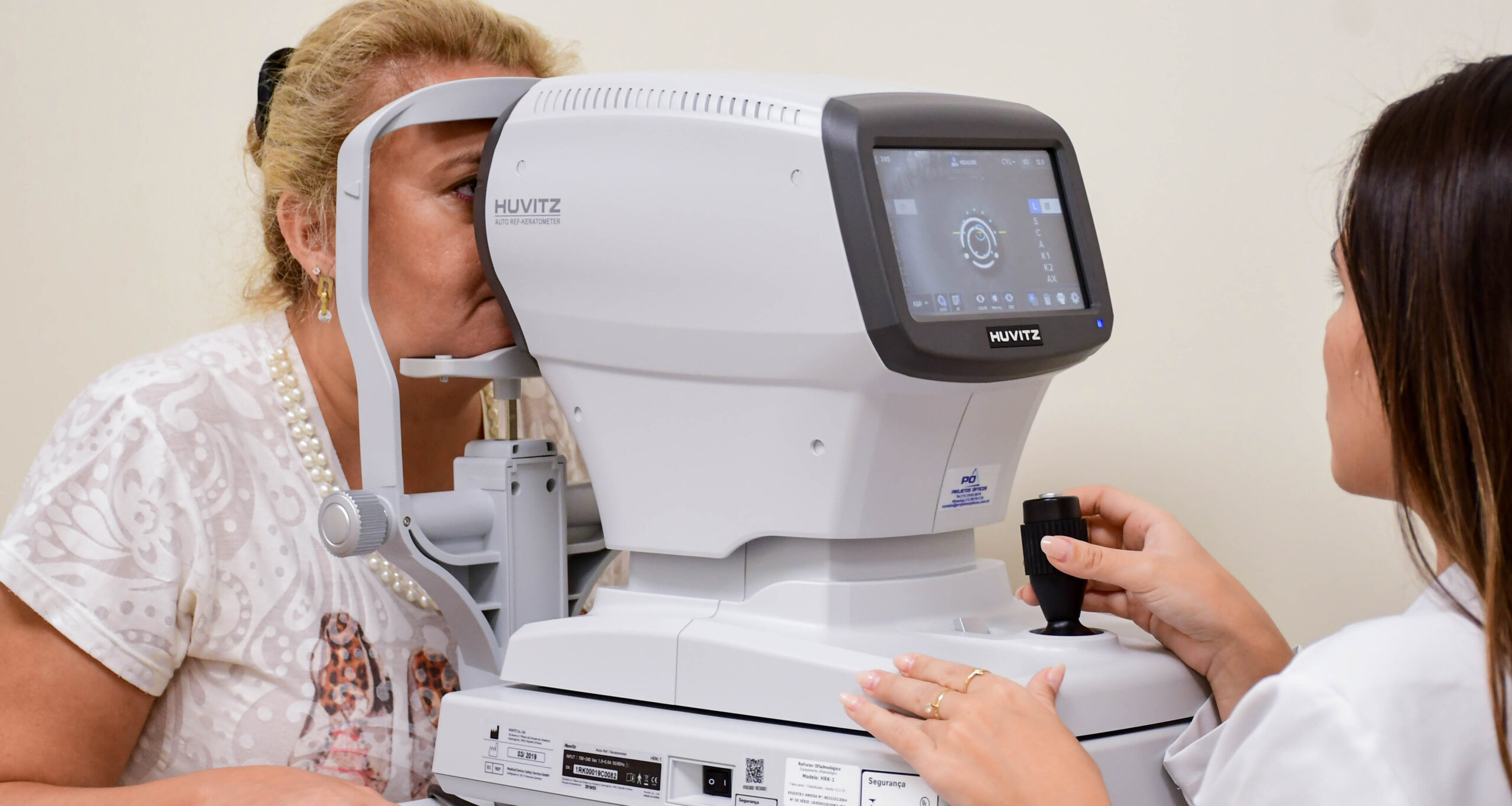 aluna de Medicina da Unoeste realiza exame de refração ocular em paciente usando um equipamento de diagnóstico visual automatizado em uma clínica de Medicina. O ambiente é limpo e bem iluminado.