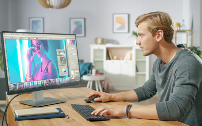 Homem loiro editando foto de mulher com óculos escuros em computador.