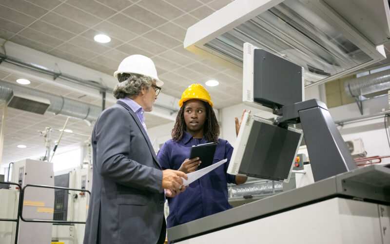 Engenheira e gerente discutindo operação de máquina industrial.