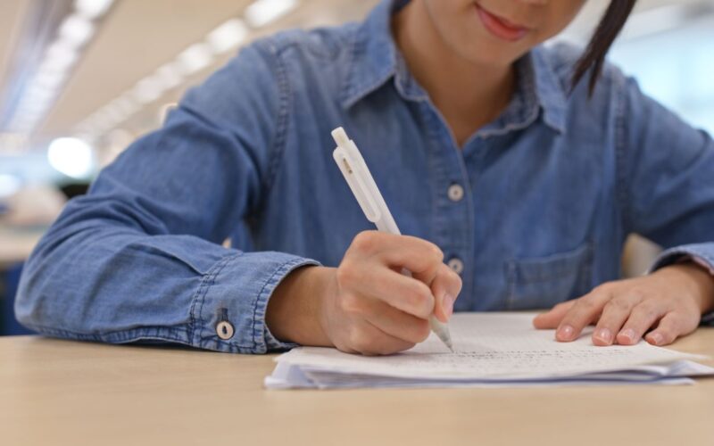 Estudante escrevendo em folha sobre tema de redação para o Enem.