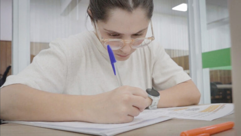 Estudante concentrada fazendo anotações em caderno durante os estudos para o Enem, com materiais de apoio e marca-texto sobre a mesa.
