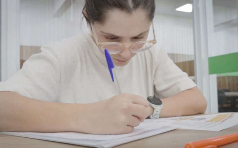 Estudante concentrada fazendo anotações em caderno durante os estudos para o Enem, com materiais de apoio e marca-texto sobre a mesa.