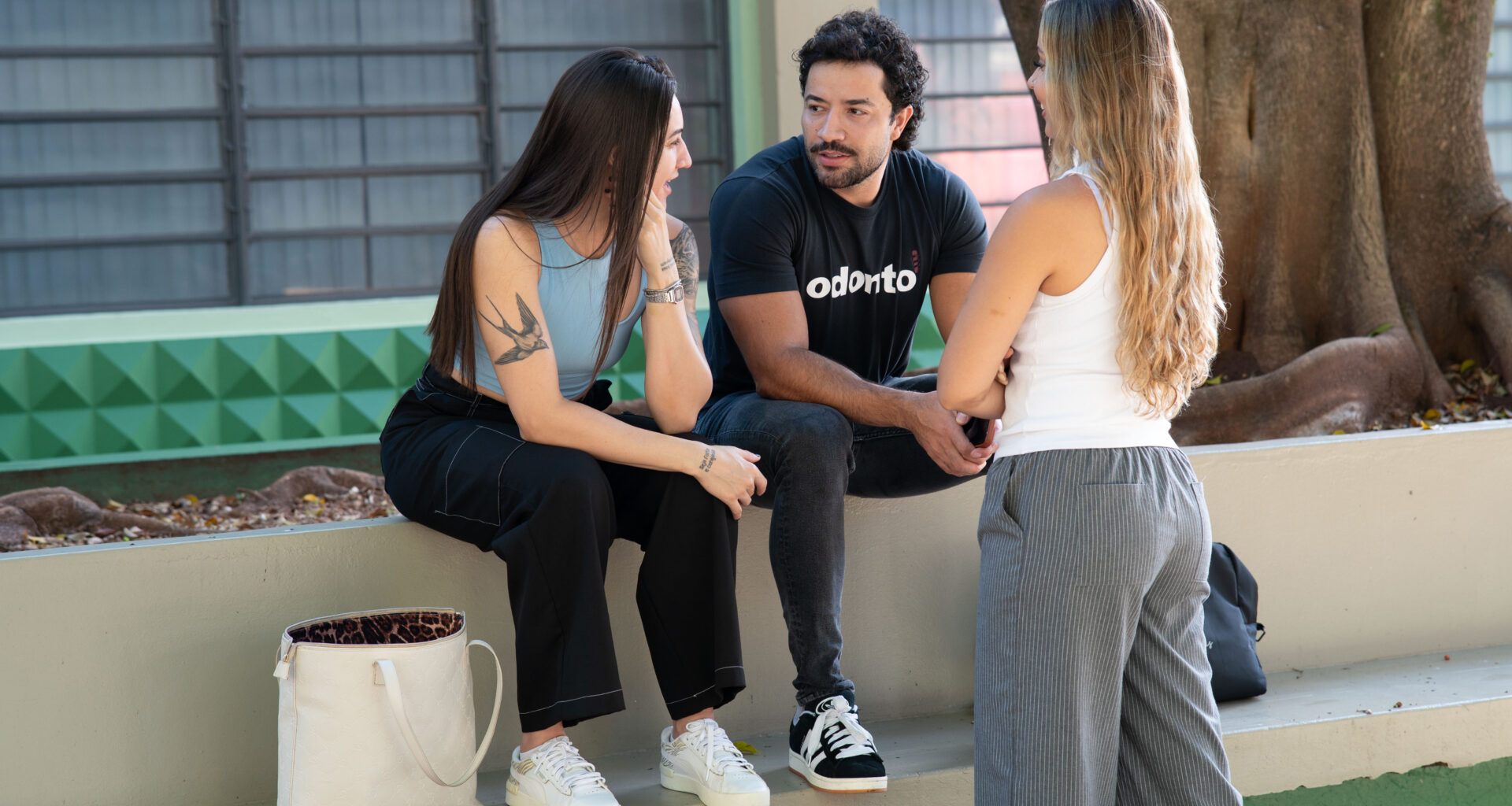 Três estudantes universitários conversam ao ar livre em área de convivência do campus, trocando experiências e discutindo sobre escolhas profissionais e a vida acadêmica.