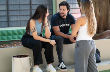 Três estudantes universitários conversam ao ar livre em área de convivência do campus, trocando experiências e discutindo sobre escolhas profissionais e a vida acadêmica.