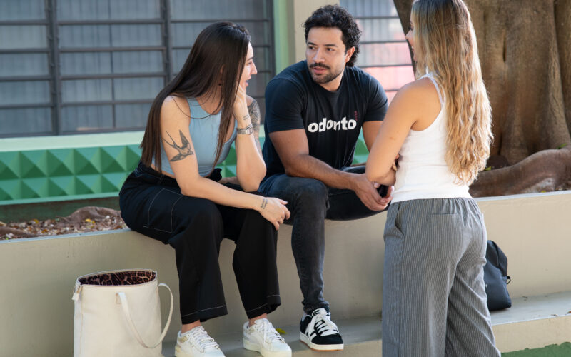 Três estudantes universitários conversam ao ar livre em área de convivência do campus, trocando experiências e discutindo sobre escolhas profissionais e a vida acadêmica.