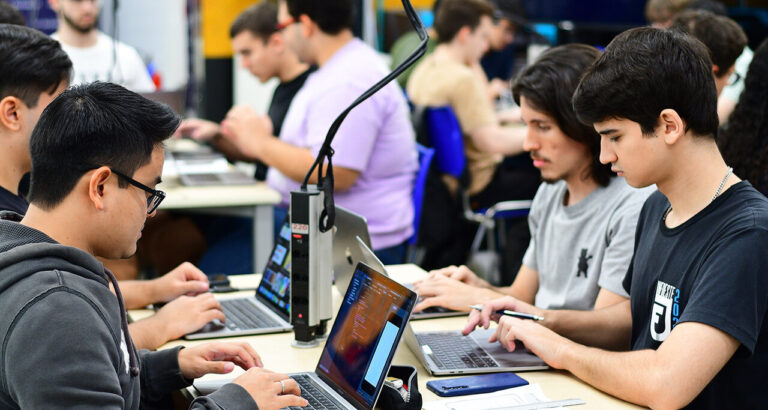 Estudantes do curso de Sistemas de Informação da Unoeste trabalhando em laboratório de informática, utilizando notebooks para atividades práticas de programação e desenvolvimento de sistemas.