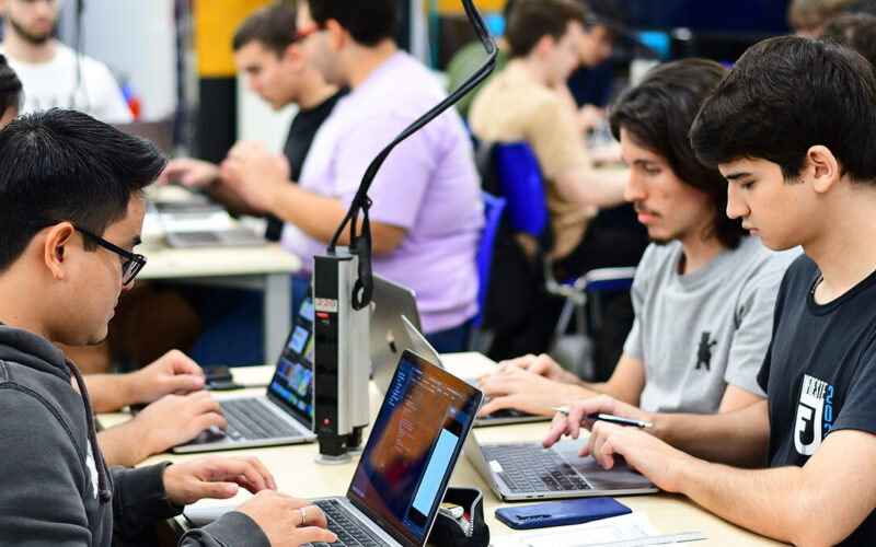 Estudantes do curso de Sistemas de Informação da Unoeste trabalhando em laboratório de informática, utilizando notebooks para atividades práticas de programação e desenvolvimento de sistemas.