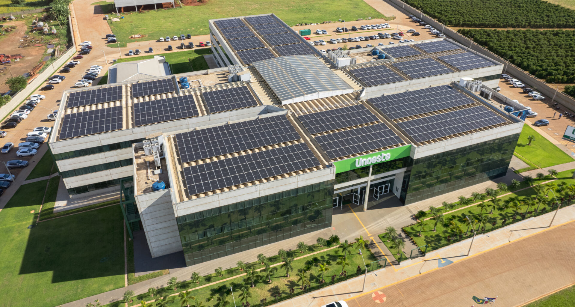 Imagem aérea do campus da Unoeste em Jaú, SP, destacando o prédio moderno com painéis solares no telhado, áreas verdes bem cuidadas ao redor e amplo estacionamento. Uma estrutura que reflete sustentabilidade e excelência acadêmica.