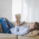 Mulher relaxando em um sofá enquanto lê um livro de romance com médico. O ambiente é iluminado e aconchegante, representando momentos de leitura e descanso.