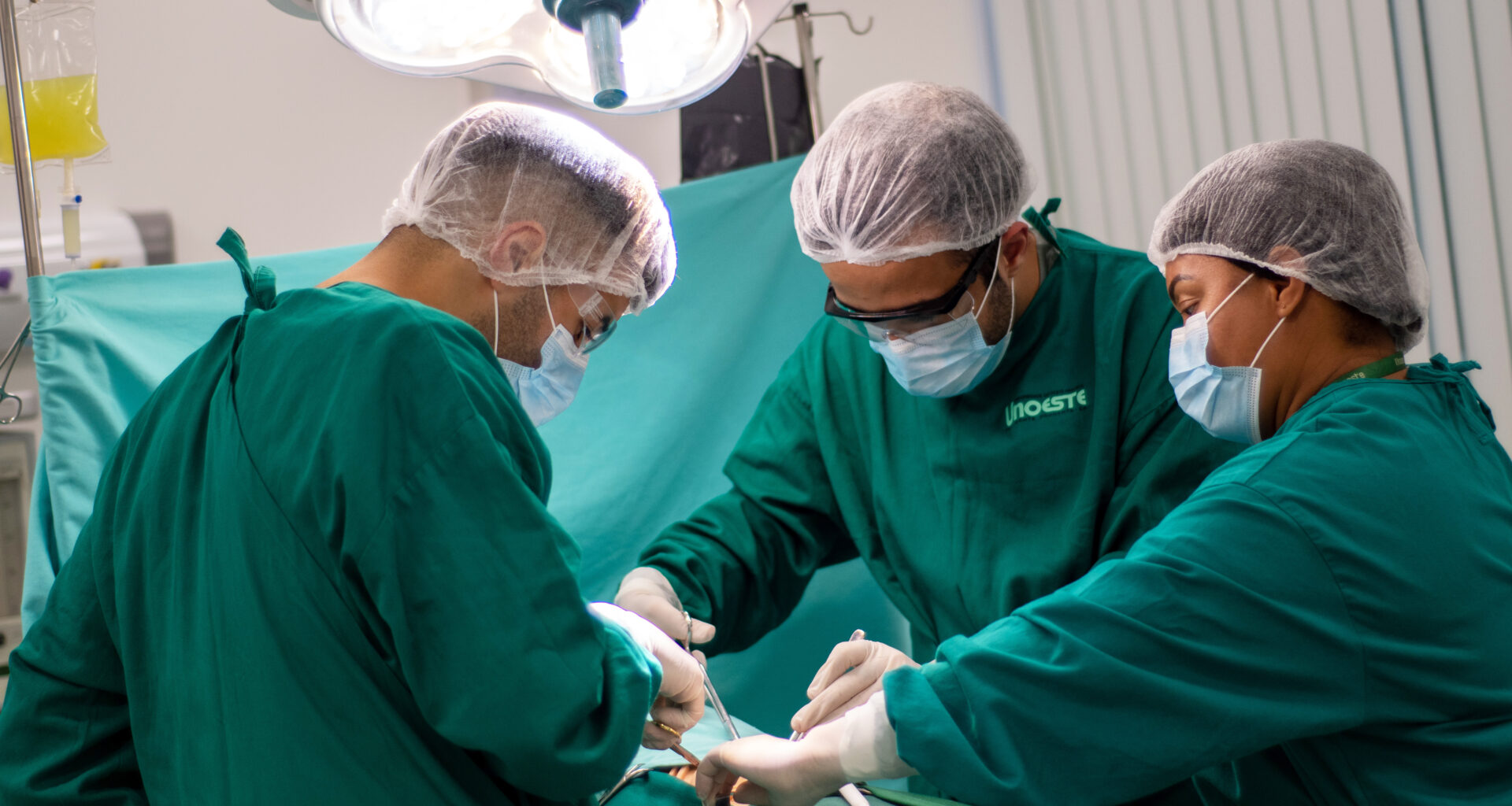 Alunos do curso de Medicina da Unoeste participando de uma aula prática em um laboratório de simulação cirúrgica, utilizando trajes e equipamentos adequados para procedimentos médicos.