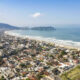 Vista aérea de Guarujá, destacando a Praia da Enseada com sua extensa faixa de areia e mar azul. A imagem revela a combinação de áreas residenciais e prédios à beira-mar, evidenciando o estilo de vida praiano da região.