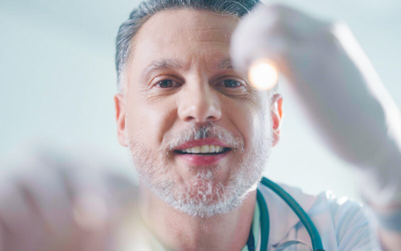 Médico realizando exame clínico com luz de diagnóstico. A evolução da medicina, dos tratamentos antigos às tecnologias modernas, transformou os cuidados com a saúde.