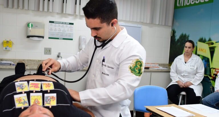 Estudante de Medicina realiza exame físico com estetoscópio em paciente durante aula prática, com supervisão docente em laboratório de simulação clínica.
