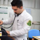 Estudante de Medicina realiza exame físico com estetoscópio em paciente durante aula prática, com supervisão docente em laboratório de simulação clínica.