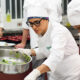 Estudantes do curso de Gastronomia da Unoeste preparam e finalizam pratos em aula prática de cozinha, vestindo uniformes completos e atuando em equipe.