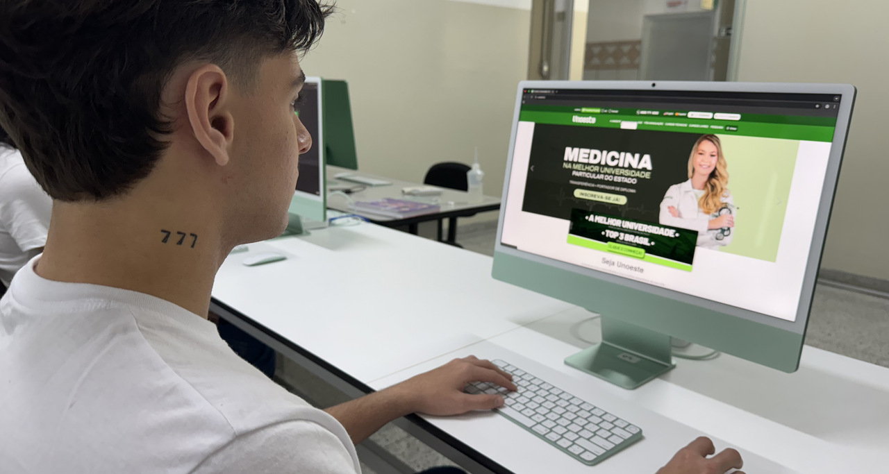 Estudante jovem acessa o site da Unoeste em um computador, visualizando informações sobre o Vestibular de Medicina. A imagem representa o interesse de adolescentes em começar a faculdade e buscar informações sobre vestibulares.