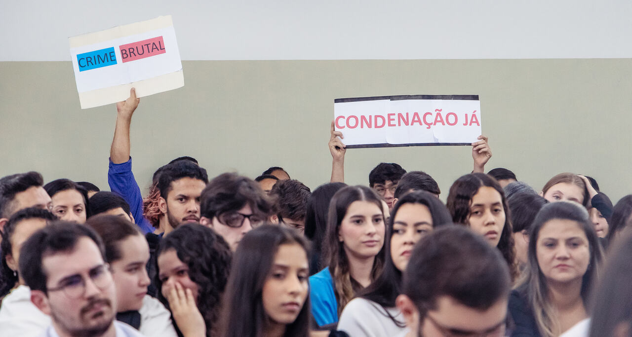 Público assiste simulação de julgamento com cartazes “Crime brutal” e “Condenação já” erguidos por participantes, em atividade acadêmica do curso de Direito da Unoeste.