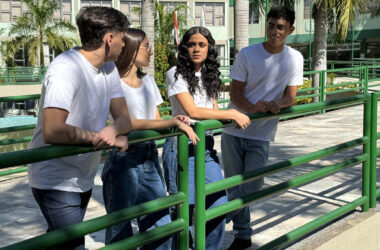 Quatro estudantes universitários conversam ao ar livre no campus da Unoeste, cercados por palmeiras e edifícios modernos, vestindo camisetas brancas e calças jeans, em um ambiente descontraído e acolhedor.