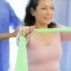Mulher realizando exercício com faixa elástica durante sessão de fisioterapia, acompanhada por profissional da área da saúde. Técnica utilizada na Reeducação Postural Global (RPG).