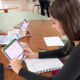Estudantes utilizando tablets e cadernos durante rotina de estudos em ambiente universitário, com foco em preparação para redação e provas.