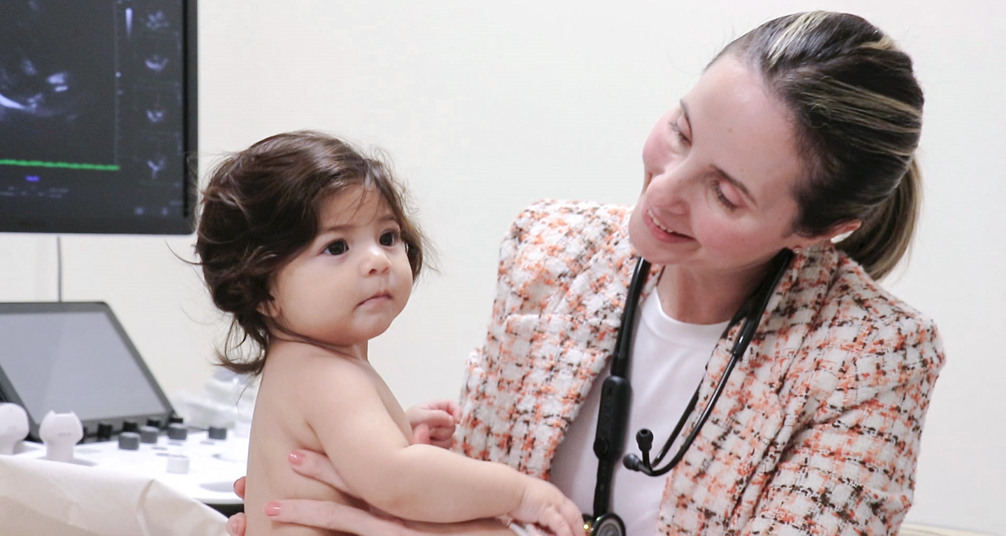 Uma médica atenciosa interage com um bebê em um ambiente clínico, com equipamentos médicos ao redor. A dedicação profissional é evidente, e a estabilidade de carreira, muitas vezes buscada em um concurso médico, é um atrativo para a profissão.