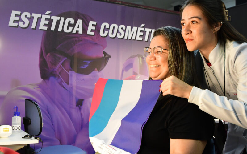 Aluna do curso de Estética e Cosmética da Unoeste orienta visitante durante feira de profissões, mostrando possibilidades da carreira na área da beleza e bem-estar.