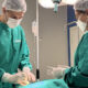 Estudante de Medicina da Unoeste realiza procedimento prático supervisionado em ambiente hospitalar, vestindo roupas cirúrgicas e máscara, durante atividade de treinamento.