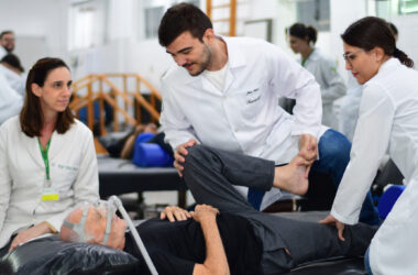 Estudantes e professora do curso de Fisioterapia da Unoeste realizam atendimento a paciente idoso utilizando técnicas de reabilitação física em ambiente clínico universitário.