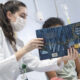 Estudante da Unoeste com jaleco branco lê um livro infantil para uma criança em ambiente hospitalar durante atividade do Projeto Leia no Leito, demonstrando empatia e atuação como voluntária no cuidado humanizado.