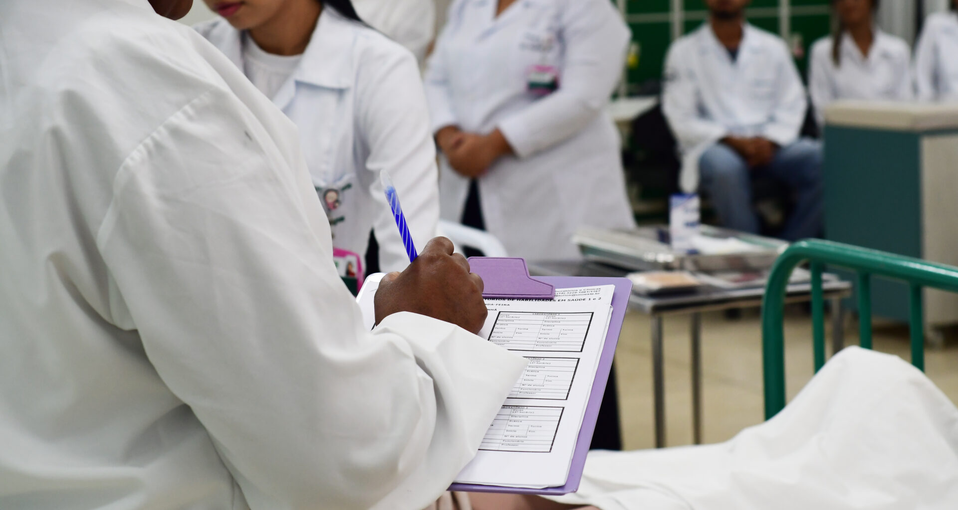 Estudante de Enfermagem da Unoeste realizando anotações de Enfermagem em prontuário durante atendimento, prática essencial para registro de cuidados e comunicação entre a equipe hospitalar.