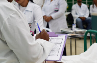 Estudante de Enfermagem da Unoeste realizando anotações de Enfermagem em prontuário durante atendimento, prática essencial para registro de cuidados e comunicação entre a equipe hospitalar.