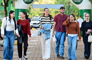 Estudantes caminham juntos pelo campus da Unoeste, em área externa sinalizada com bandeiras da universidade.