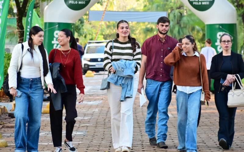 Estudantes caminham juntos pelo campus da Unoeste, em área externa sinalizada com bandeiras da universidade.