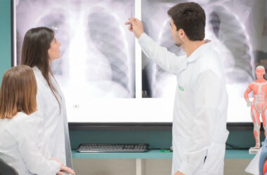 Estudantes de Medicina da Unoeste em laboratório, vestidos de jaleco branco, analisando imagens de raio-x em tela e discutindo diagnósticos clínicos, com materiais anatômicos de apoio no ambiente.