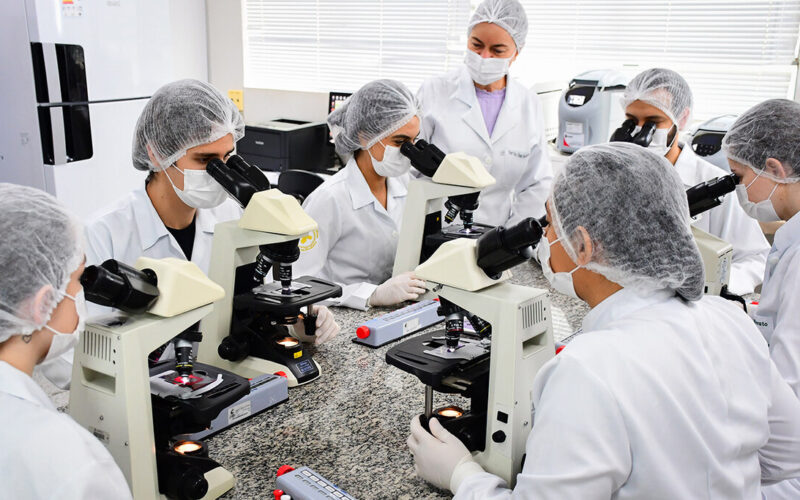 Estudantes do curso de Biomedicina da Unoeste realizam atividades práticas de análises clínicas em laboratório moderno, utilizando microscópios e aplicando técnicas laboratoriais essenciais para a formação em uma das principais áreas da saúde.